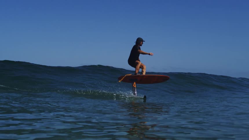 A hydrofoil surfer glides effortlessly across a calm ocean wave in stunning slow motion as the camera sinks below the surface