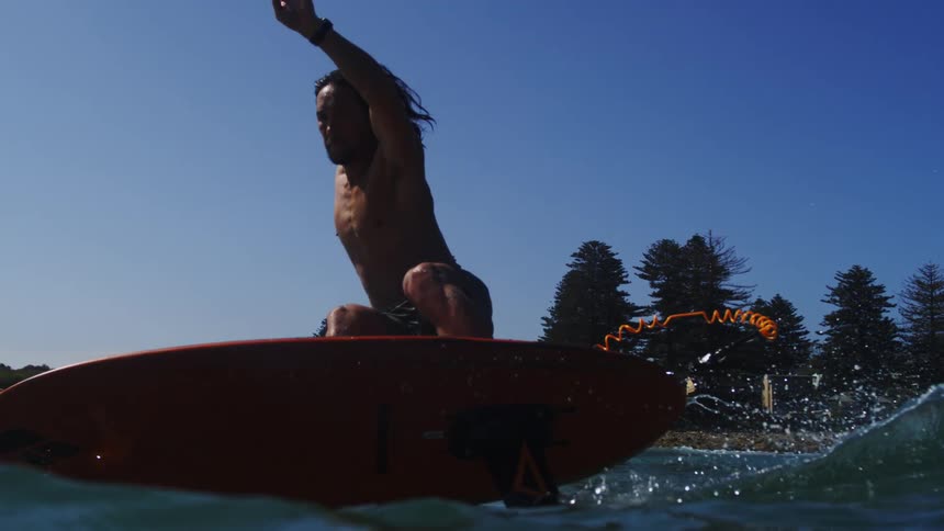 A man skillfully balances on a hydrofoil surfboard in slow motion before turning and splashing into the ocean on a sunny day