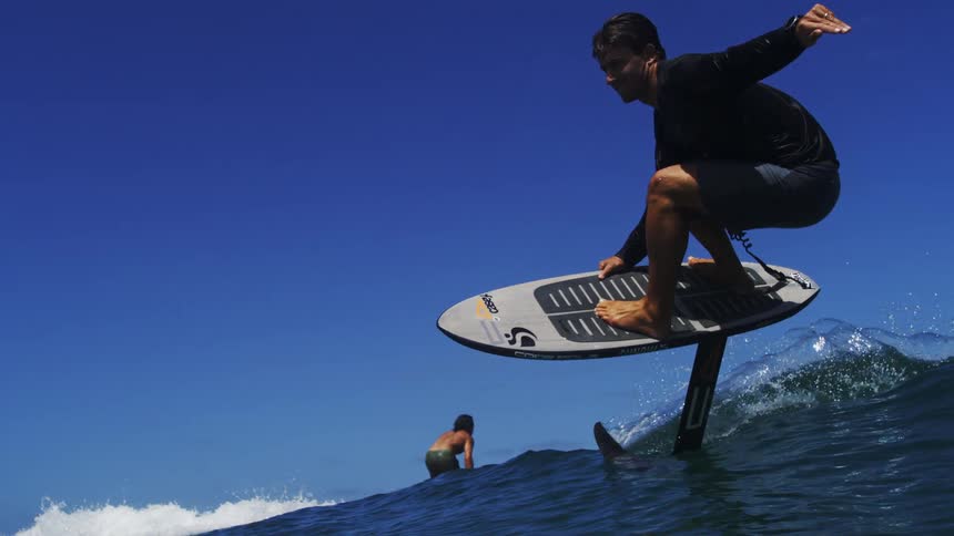 A surfer skillfully glides across an ocean wave on a hydrofoil board in super slow motion on a beautiful sunny day