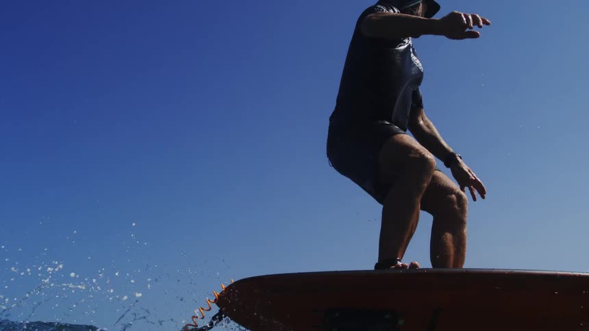 A man skillfully hydrofoil surfs in slow motion, gliding gracefully over the ocean waves towards a sandy beach on a sunny day