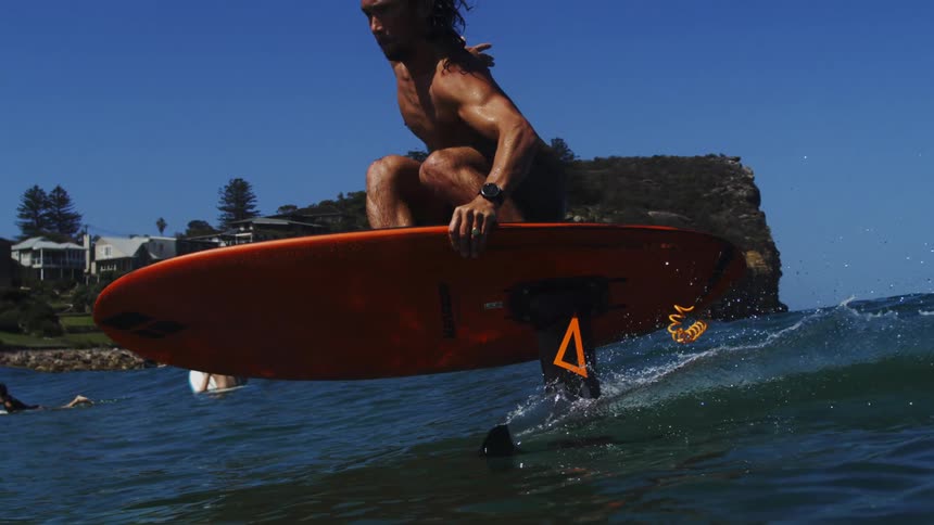 An athletic man with long hair skillfully rides a hydrofoil surfboard across the calm ocean in super slow motion on a bright sunny day