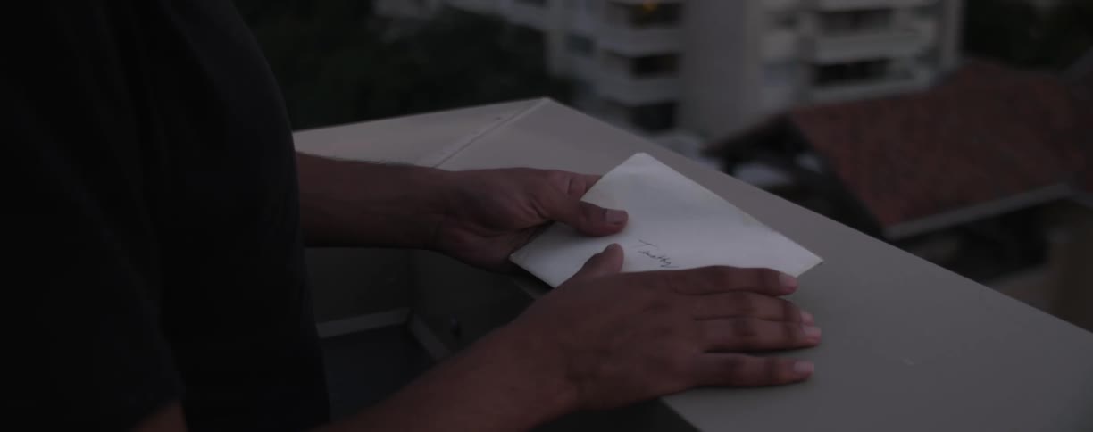 Person turns an envelope over in his hands while leaning over a balcony edge
