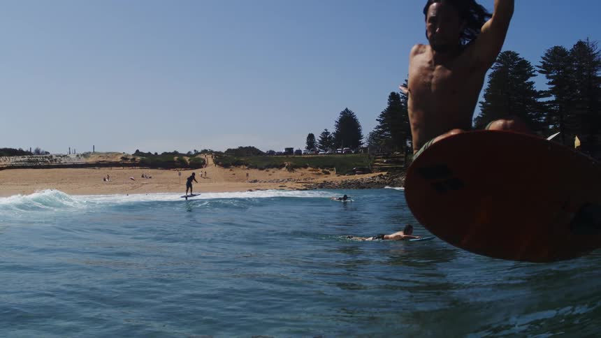 Slow motion shot of a man hydrofoil surfing on a beautiful day, riding a wave before gracefully falling into the water