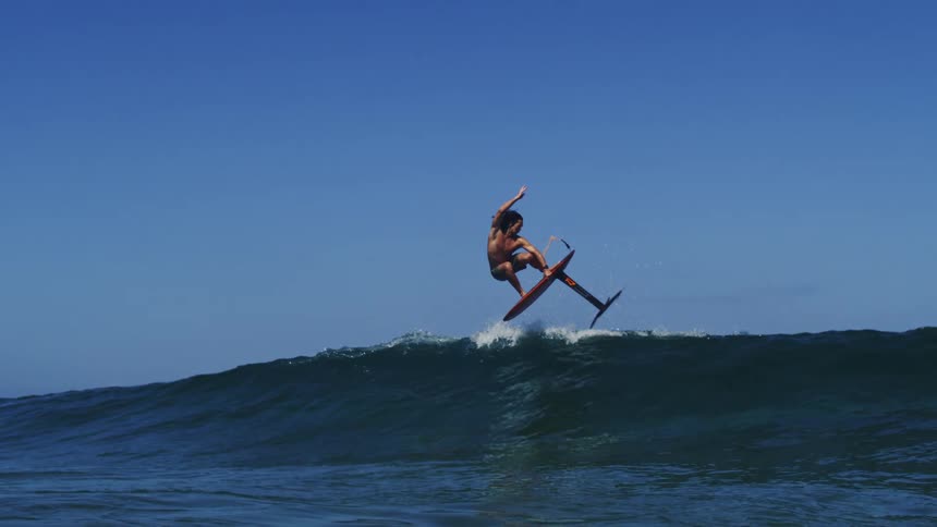 An amazing slow motion shot of a hydrofoil surfer flying out of the water and riding a wave on a sunny day