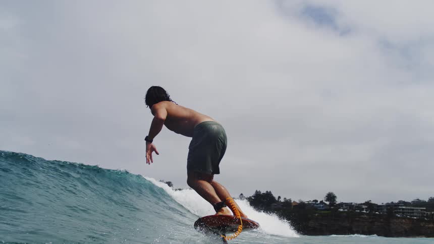 A surfer skillfully glides across a rolling ocean wave on a hydrofoil surfboard in dramatic slow motion