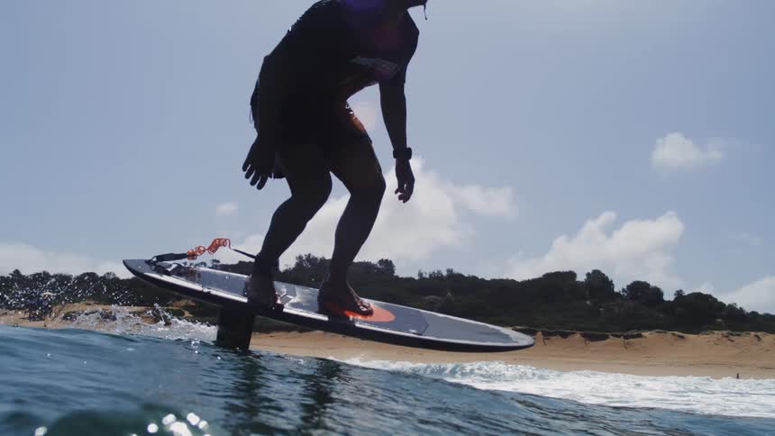 Slow motion water-level view of a surfer skillfully riding a hydrofoil board on a sunny day at the beach