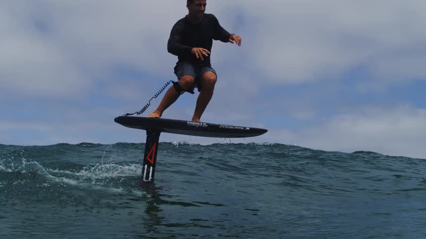 A surfer skillfully rides an electric hydrofoil surfboard, gliding smoothly above the ocean's surface in stunning slow motion
