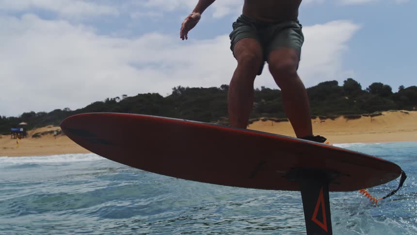 A man skillfully glides across the water on an electric hydrofoil surfboard in an impressive slow-motion shot