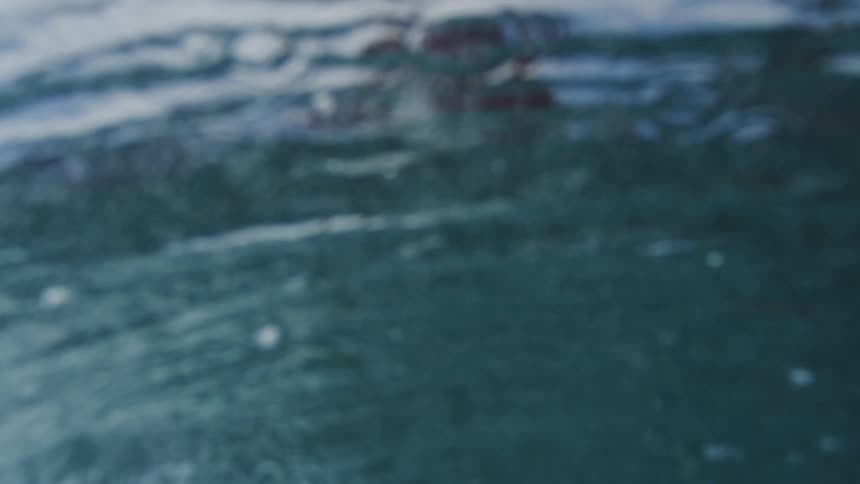 Slow motion, water-level view of a surfer gliding on a hydrofoil board along a wave, ending with an underwater perspective