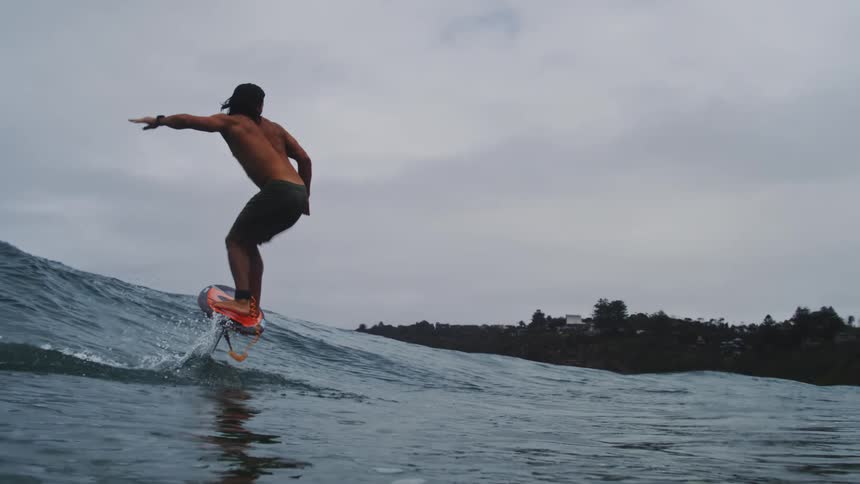 A man skillfully hydrofoil surfs on an ocean wave in dramatic slow motion under an overcast sky