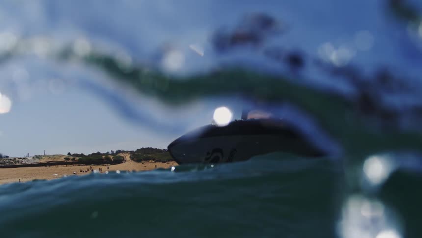 Slow motion shot of a man riding an electric hydrofoil surfboard across the ocean on a bright sunny day