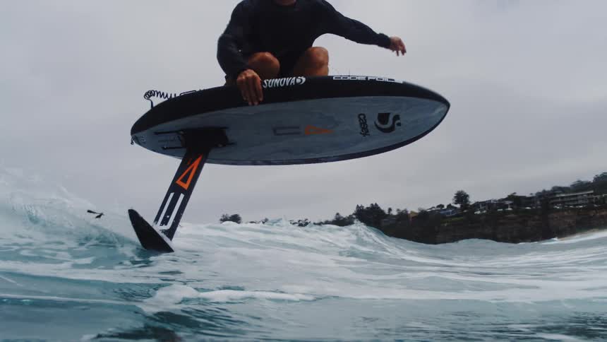 An expert surfer gracefully rides a wave on an electric hydrofoil surfboard in dramatic super slow motion