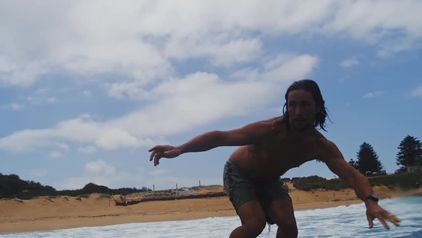 An athletic long-haired man skillfully rides a wave on a hydrofoil surfboard in a super slow-motion close-up