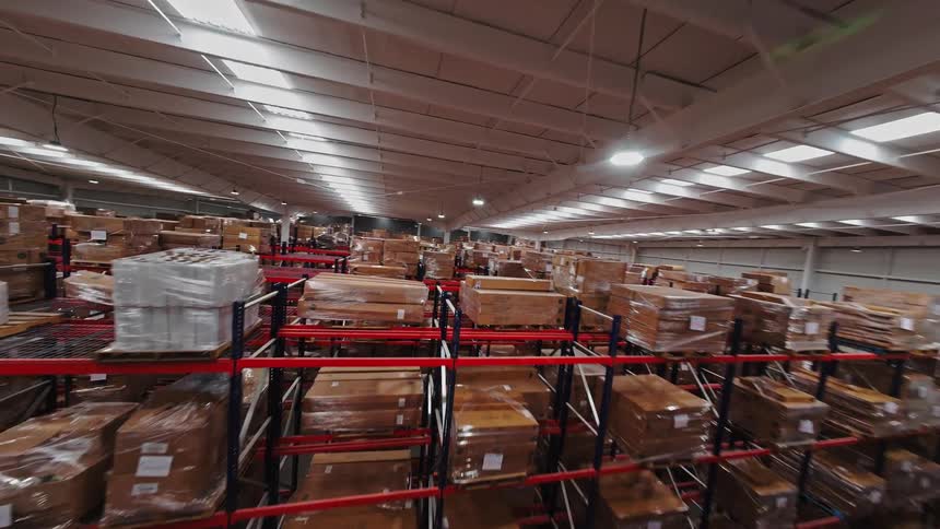 An FPV drone flies over the top shelves of a massive, well-stocked warehouse, revealing endless aisles of inventory