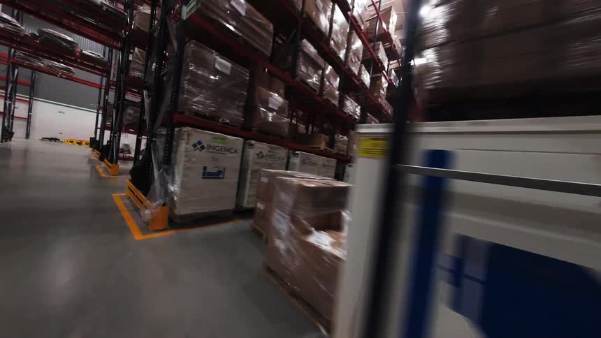 Smooth point-of-view shot traveling down the aisles of a massive industrial warehouse filled with tall shelves of merchandise