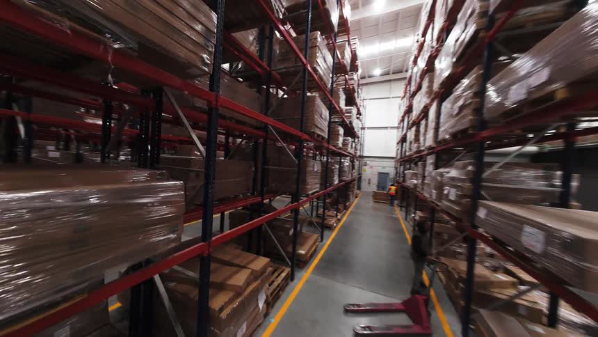 Dynamic FPV drone footage glides through the aisles of a massive, modern warehouse with towering shelves full of inventory