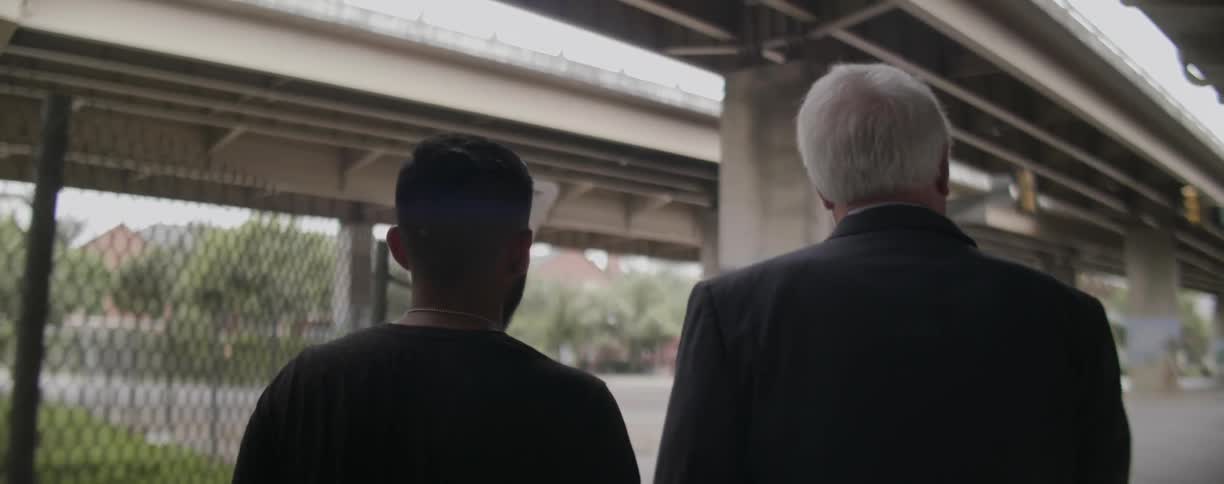Two men walk beneath overpasses in a city