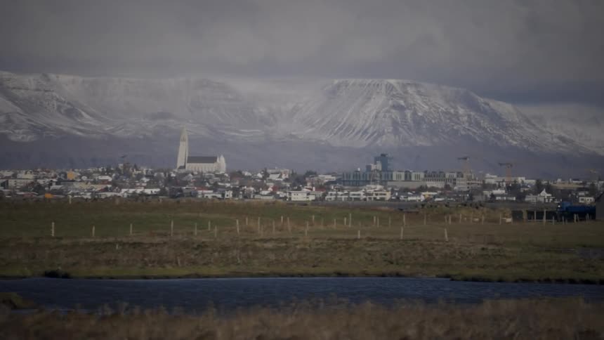 A distant wide shot of Reykjavik, Iceland, with the iconic Hallgrímskirkja church standing out against a backdrop of snow-covered mountains