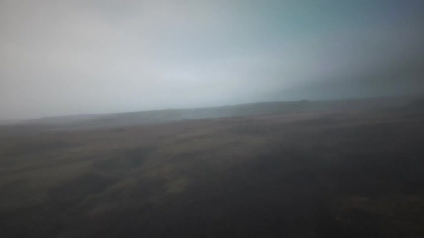 A slow and eerie aerial flight over a desolate, foggy moorland landscape