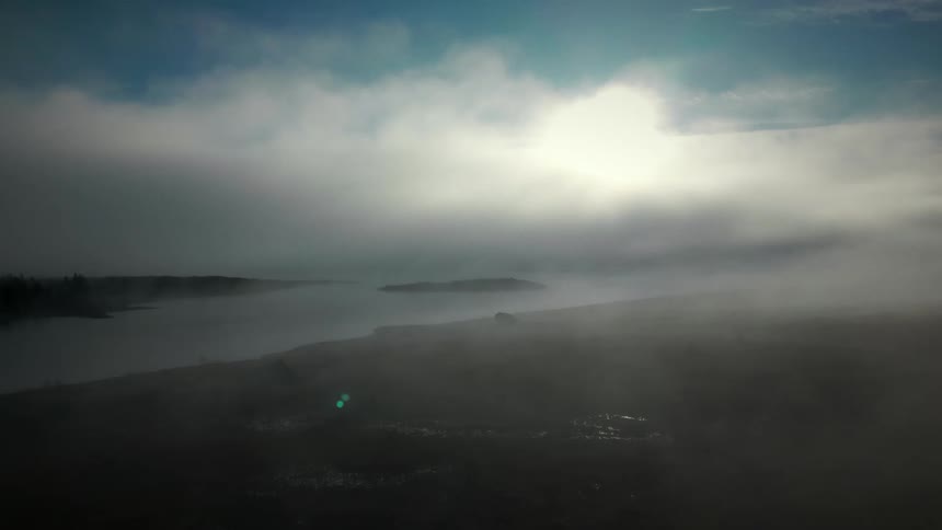 Majestic aerial view of a lake and hillside shrouded in thick morning fog with the sun glowing brightly