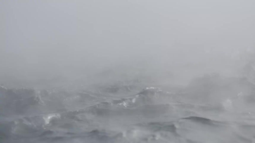 Intense steam and mist rise from the choppy surface of a frigid sea during a fierce winter blizzard