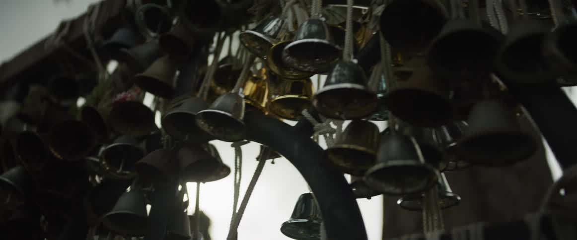 A close-up slow pan reveals a collection of various metal bells hanging from a wooden structure