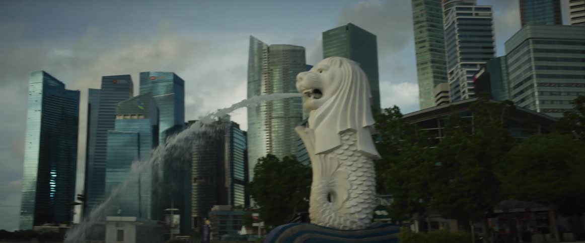 The iconic Merlion statue stands proudly spouting water as the camera pans across the magnificent modern skyline of Singapore