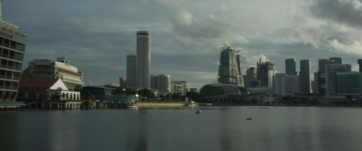 A pan across the calm waters of Marina Bay reveals the modern architecture and skyline of Singapore under a cloudy sky
