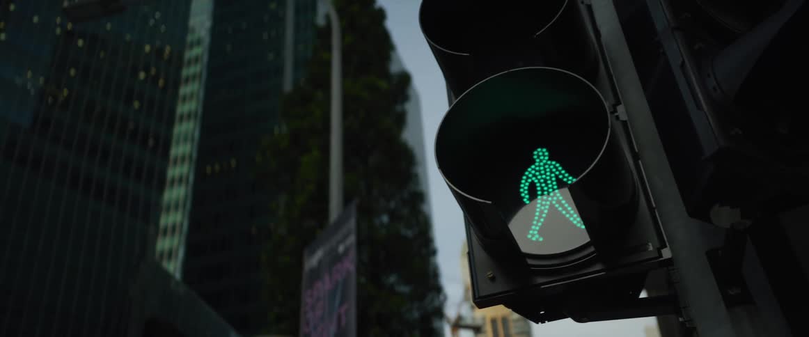 A green pedestrian walk signal glows against the backdrop of a modern city skyscraper