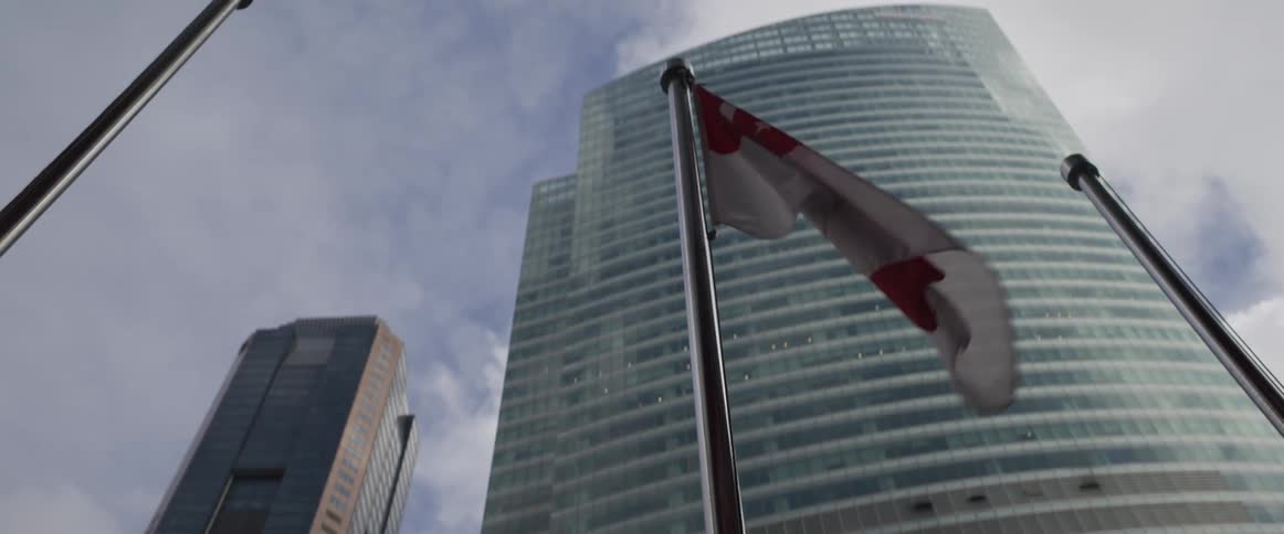 A low angle, slow-motion shot of the Singapore flag waving in front of modern glass skyscrapers