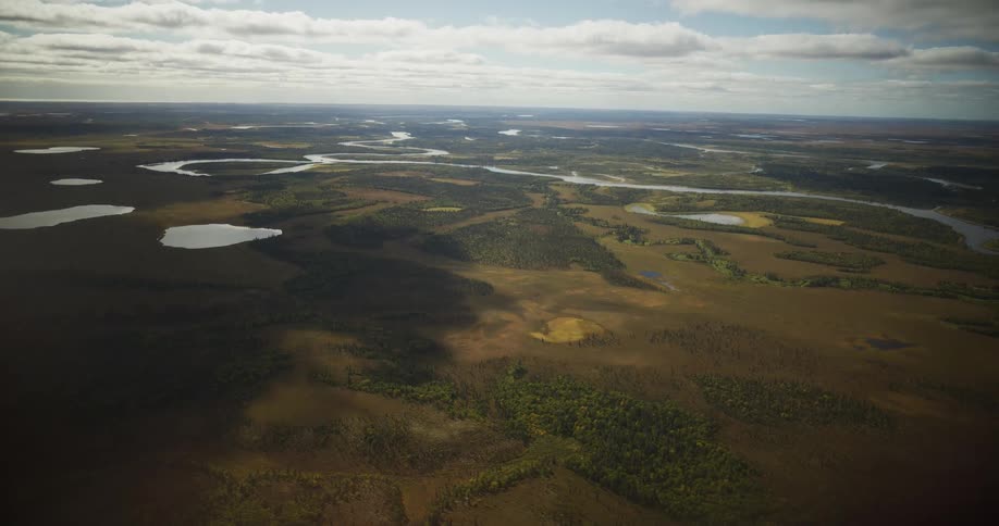 A high-angle aerial view reveals a vast, remote wilderness landscape of tundra and forests, crisscrossed by winding rivers and dotted with countless lakes under a cloudy sky