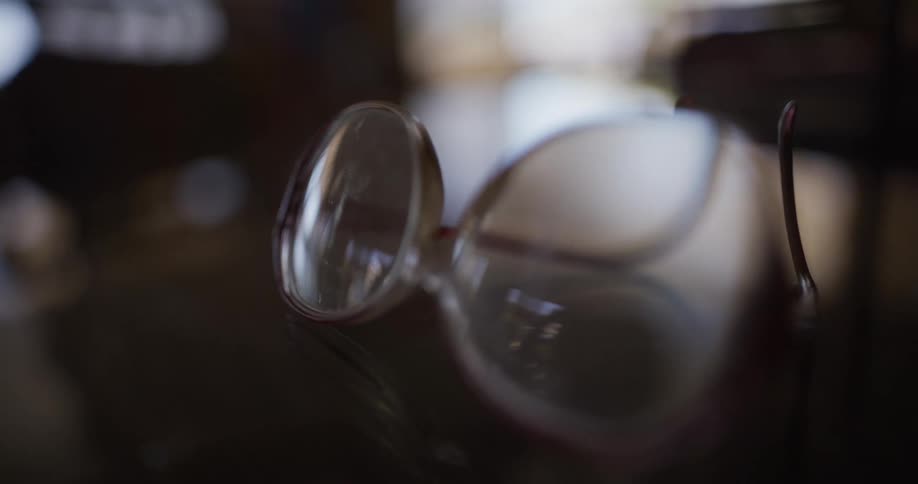 Stylish red-framed sunglasses are revealed in a slow focus pull from a tipped-over wine glass