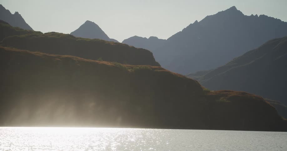 Misty haze rises from a tranquil mountain lake as sunlight reflects on the calm water