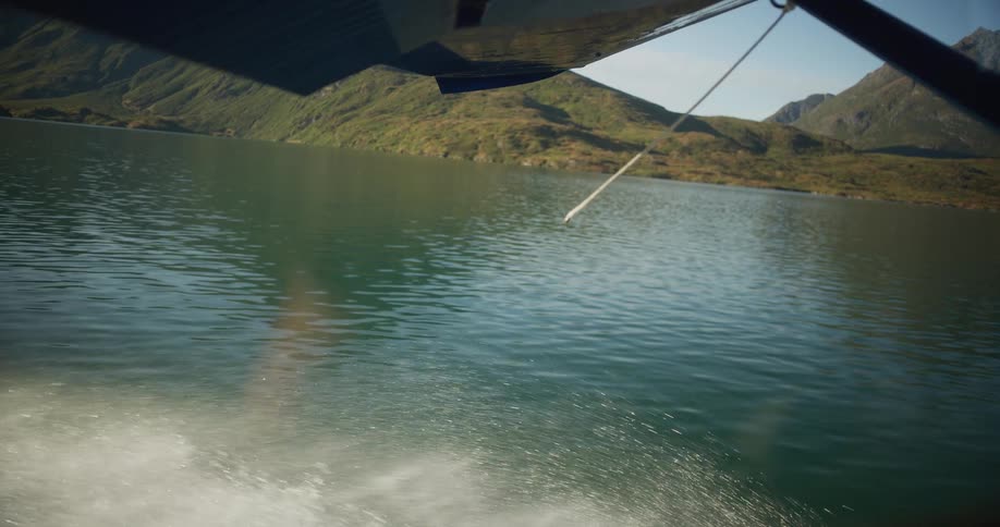 A seaplane glides across a tranquil mountain lake in slow motion, with water spraying up from its floats