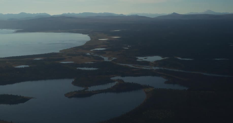 A serene aerial view shows a network of pristine lakes and rivers winding through a vast, dense forest with distant mountains on the horizon