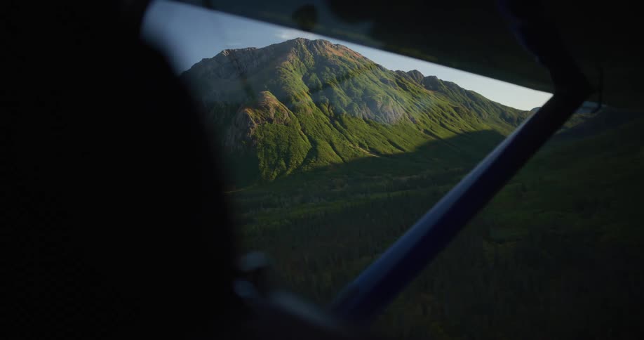 A stunning view from a small airplane window captures a majestic green mountain peak bathed in the golden light of sunset