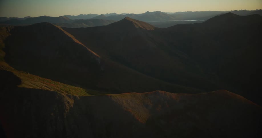 An epic aerial view reveals a vast, remote mountain range with deep shadows and sunlit ridges at sunrise