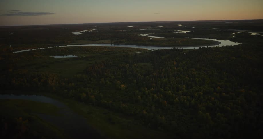 A stunning high-angle aerial view of a meandering river snaking its way through a vast, dense evergreen forest landscape at sunset