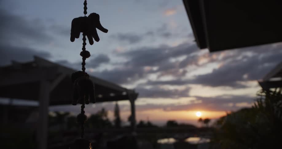 A hanging elephant ornament dangles in silhouette as the sun sets over a cloudy, tropical sky