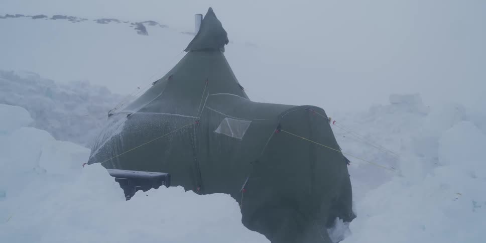 A sturdy expedition tent is buffeted by strong winds during a fierce blizzard in a desolate, snow-covered arctic landscape