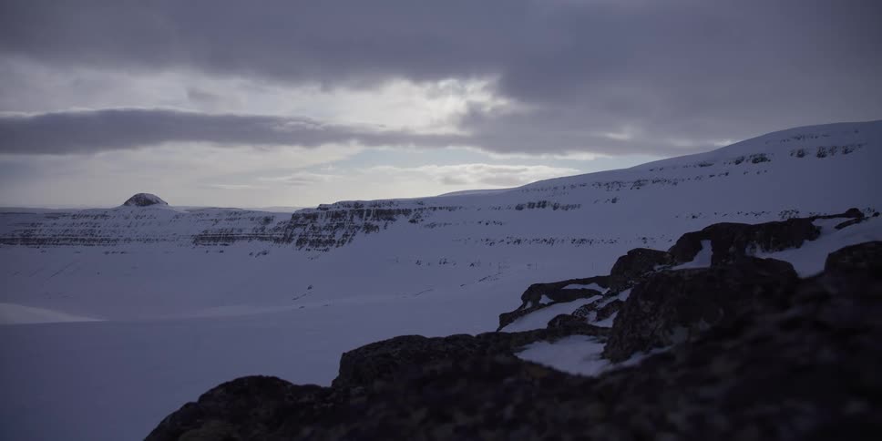 A dramatic dolly shot reveals a vast, snow-covered arctic landscape under a gloomy, overcast sky