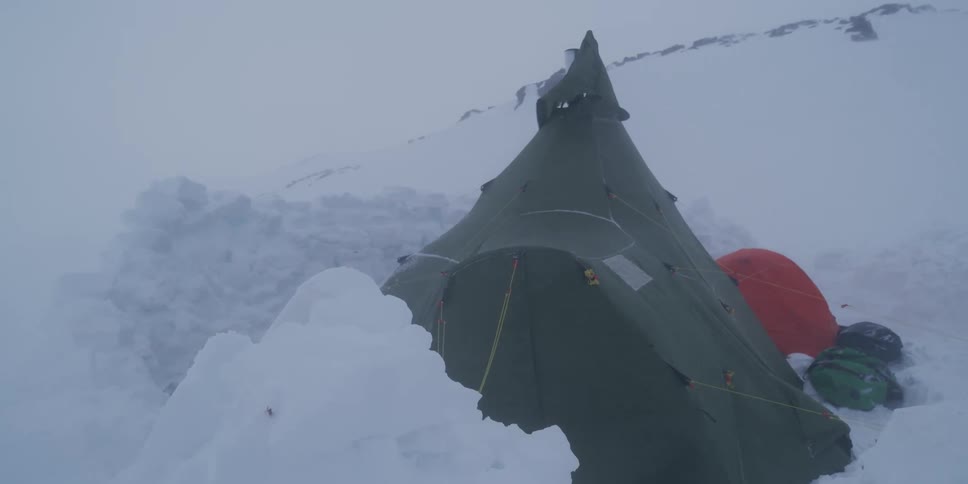 A large green expedition tent withstands a fierce blizzard on a snow-covered mountain