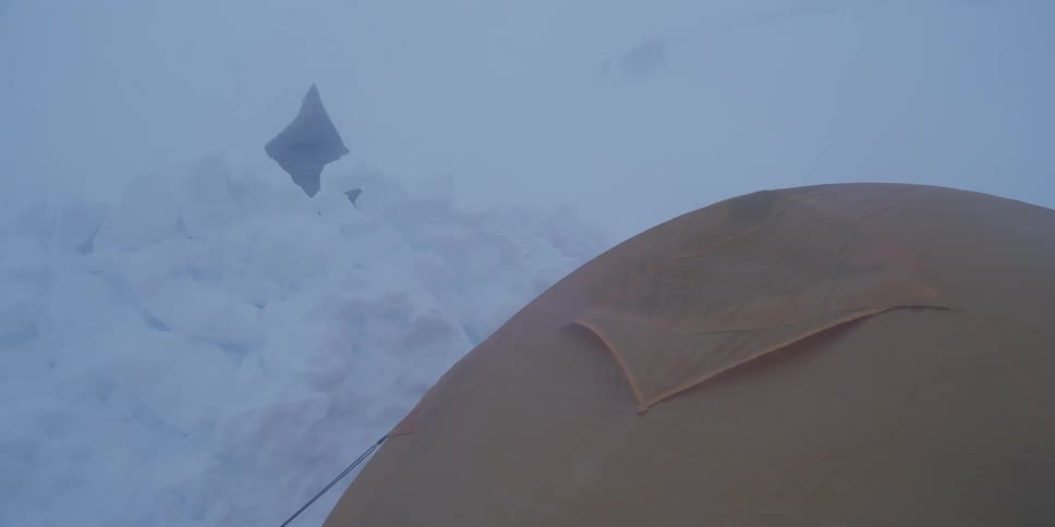 An expedition tent endures a fierce blizzard with strong winds and low visibility in the snowy mountains