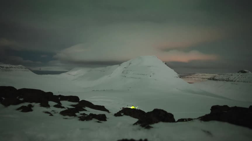 A mesmerizing night timelapse shows a remote campsite in a vast, snowy mountain valley as the Northern Lights and clouds drift across the sky