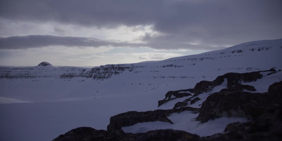 A slow dolly shot across a majestic, snow-covered mountain valley under a dramatic cloudy sky