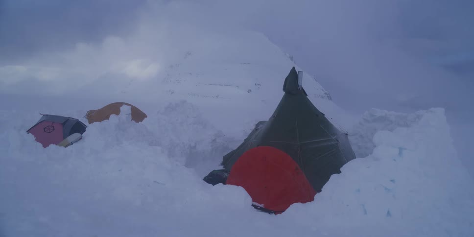 Camping tents stand against a fierce blizzard in a snowy, mountainous landscape