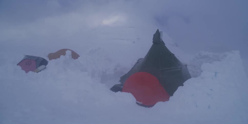 A mountain campsite with colorful tents is battered by extreme wind and snow during a blizzard