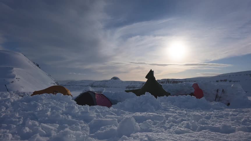 A breathtaking timelapse of a winter campsite in a snowy mountain landscape as explorers build a snow shelter