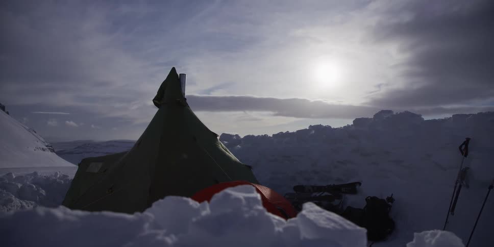 A timelapse of a remote winter basecamp with tents nestled in deep snow as the bright sun shines through passing clouds