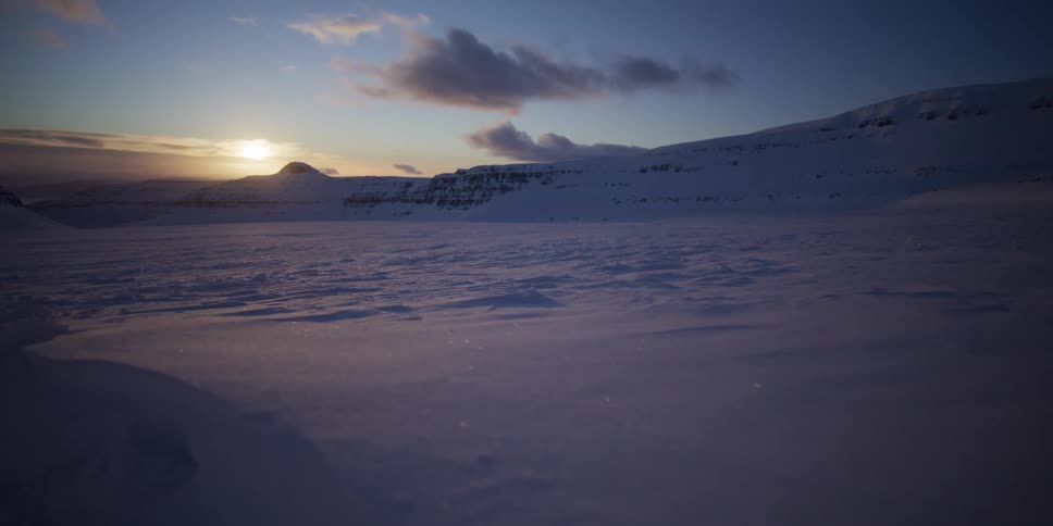 A serene tracking shot reveals a vast, glittering snowy landscape at sunset in the arctic wilderness